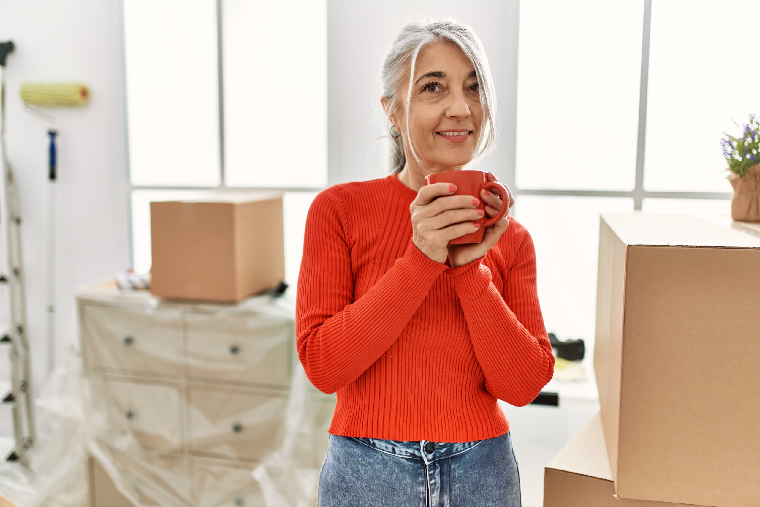 Middle age grey-haired woman smiling confident drinking coffee at new home
